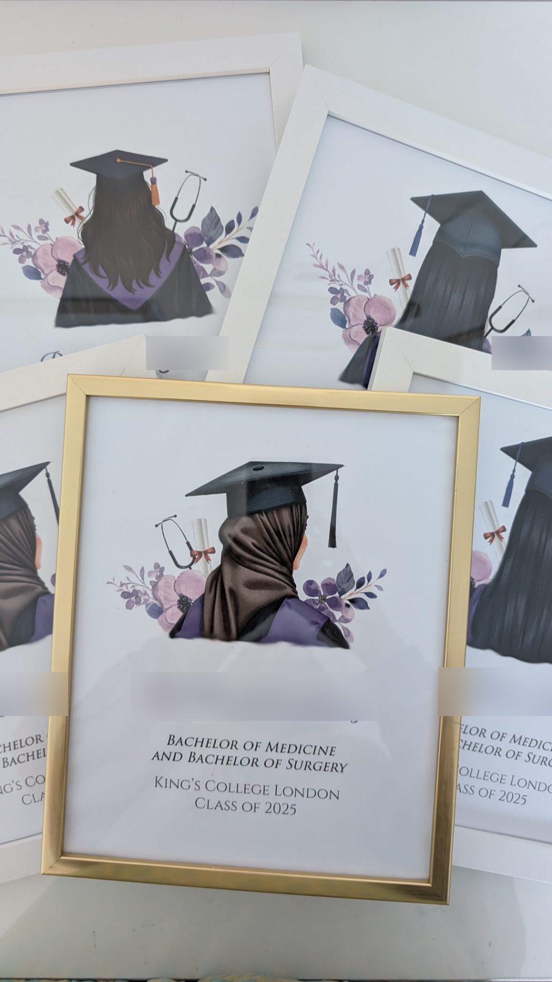 Several graduation prints in white and gold frames, stacked, one with a hijab