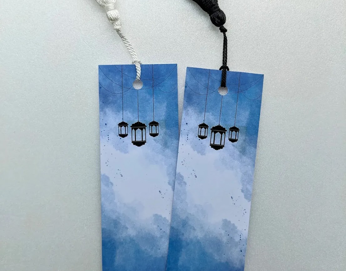Two tasselled bookmarks with a blue watercolour sky and hanging lanterns