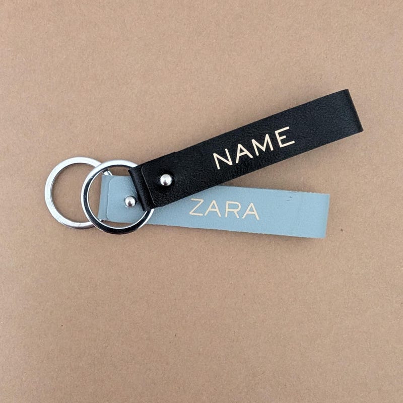 Black and pale blue faux leather keychains lettered NAME and ZARA in metallic capitals